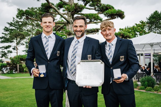 Carl Siemens, Marco Schmuck und Finn Kölle stehen im Anzug mit Anzug, Hemd und Krawatte nebeneinander und halten Medaillen in der Hand