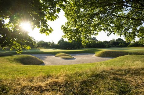 Golfbunker bei Sonnenschein mit grüner Wiese im Vordergrund