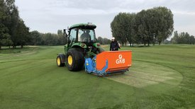 Traktor mit Anhänger fährt über Golfgrün
