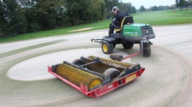 Person sitzt auf Aufsitzrasenmäher mit Anhänger und verstreut Sand auf Golfgrün