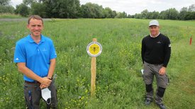 Daniel Lüttger und Karsten List stehen auf Wiese vor Schild Lebensraum Golfplatz