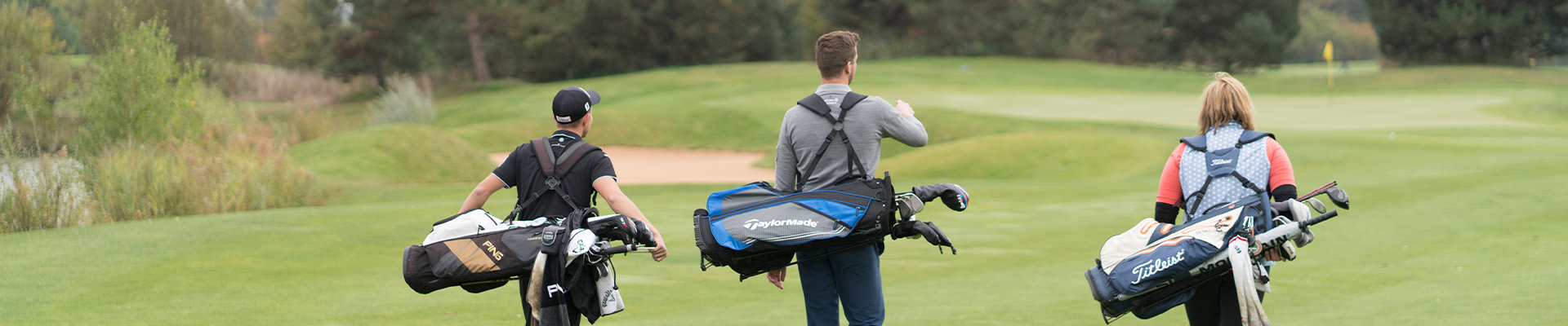 Golfer laufen auf Fairway mit umgehängten Golfbags