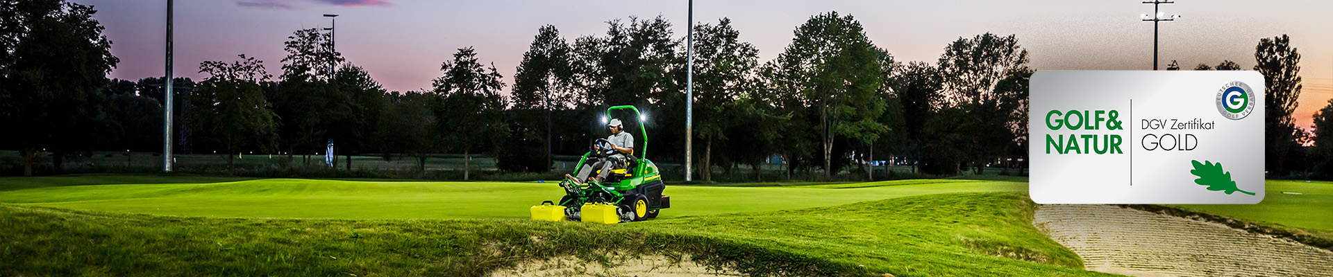 Greenkeeper fährt mit Aufsitzmäher bei Sonnenuntergang über Grünfläche