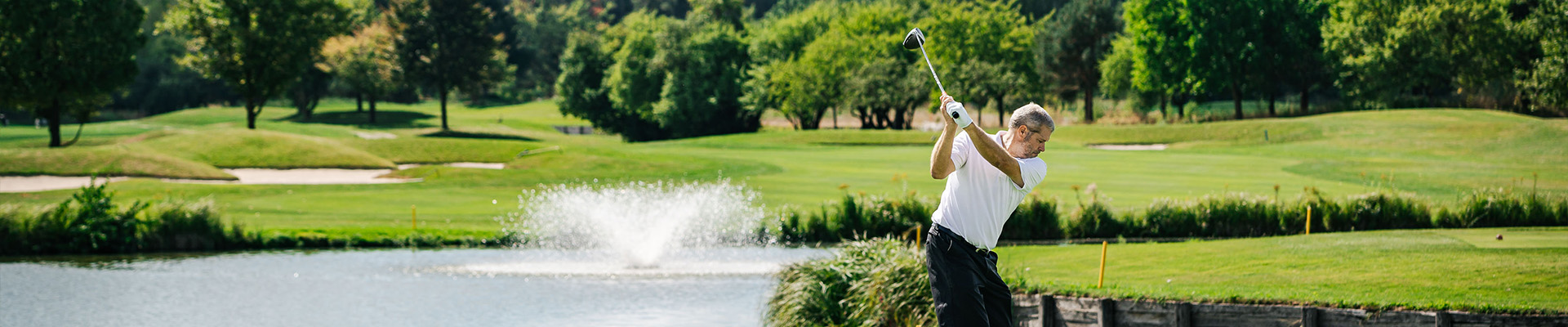Golfer beim Abschlag mit Teich im Hintergrund